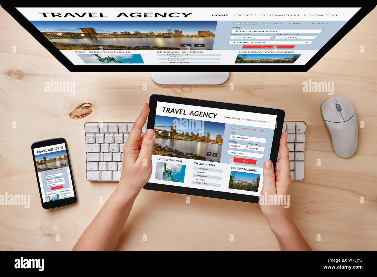 Travel agency concept on computer, tablet and smartphone screen over wooden table. Top view of responsive devices. Stock Photo