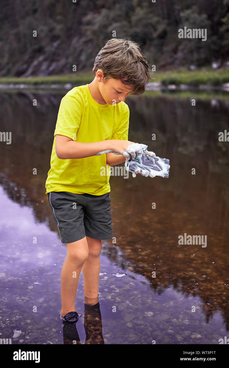 White wet boy about 8 years old is standing in river and washing mobile