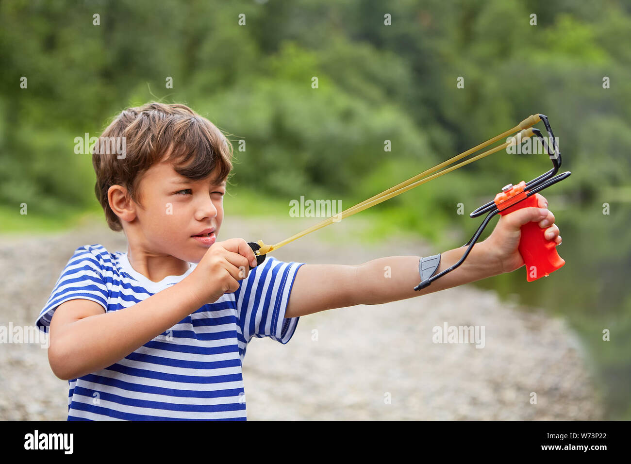 White hooligan boy in T-shirt with slingshot in his hands is preparing for shooting and finding a target. Stock Photo