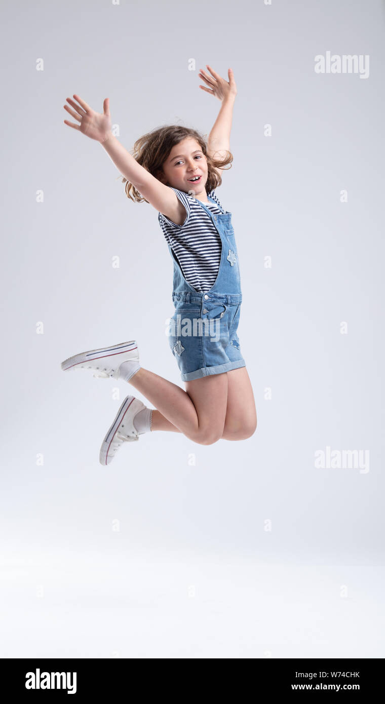 Agile energetic young girl leaping high into the air with outstretched arms looking at the camera with a smile over a white background with copy space Stock Photo