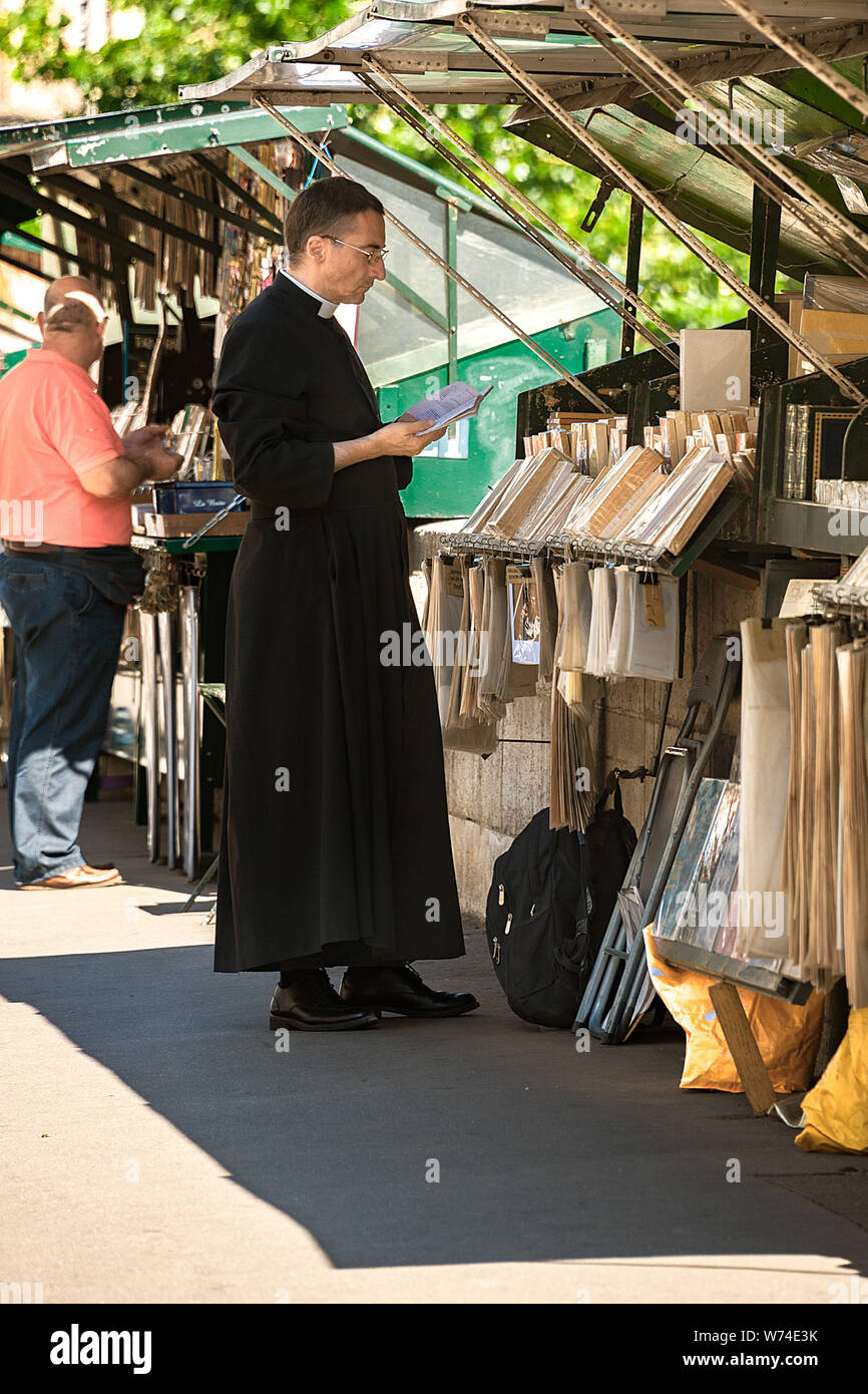 Paris, France - July 04, 2017: A priest in cassock garment glances at a book from one of the bookstalls along of River Seine sidewalk. Stock Photo