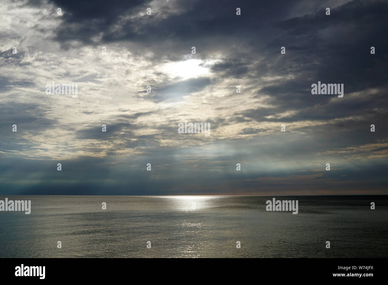 Sunset sky over the sea. The light of the sun makes its way through the clouds and the sun's rays shine above the surface of the water. Lake of Michig Stock Photo