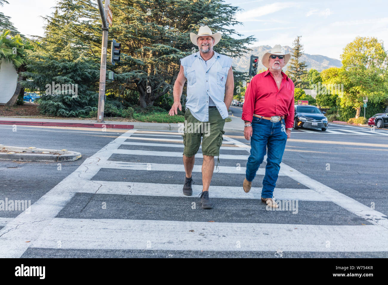 Two older male cowboys crossing State Street in Santa Barbara, California. The each wear cowboy hats, but differ in their clothing. Stock Photo