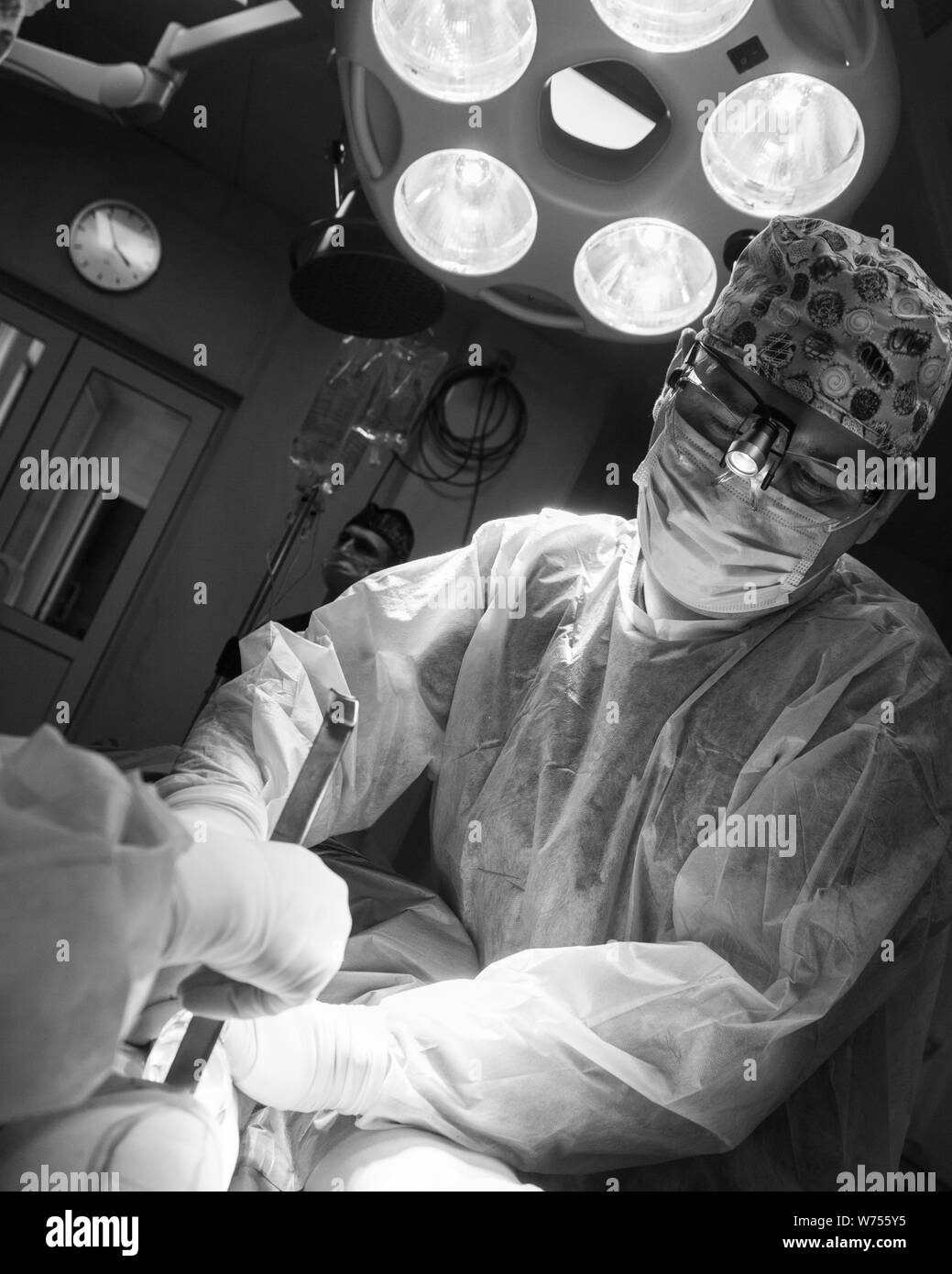 Dramatic black and white photo of the operating surgeon in the surgery room. Surgeon in mask and uniform and surgery light beside Stock Photo