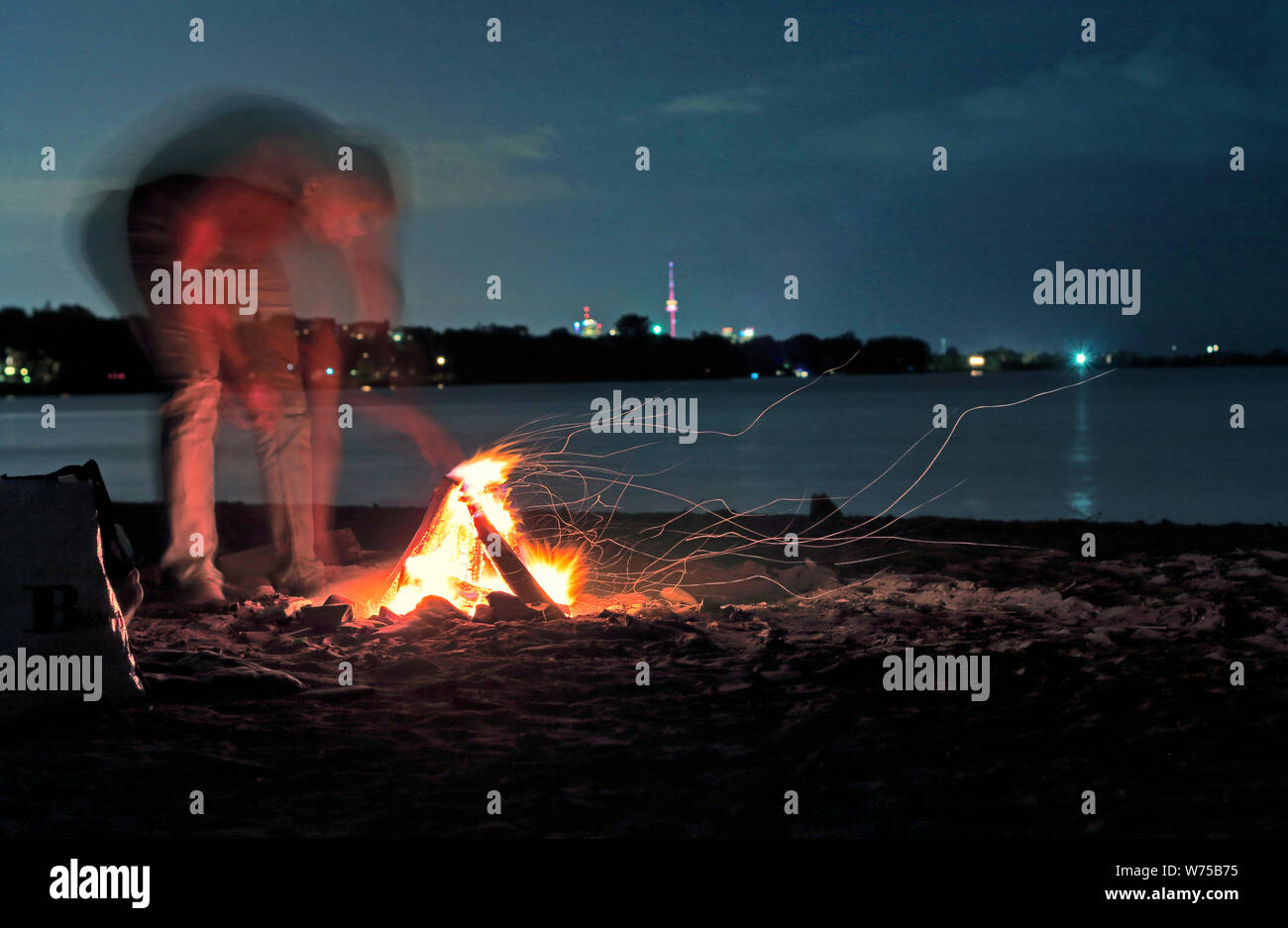 Unrecognizable person with blurred motion making beach camp fire with CN Tower along Toronto skyline by Lake Ontario under stars in the sky. Blurred m Stock Photo