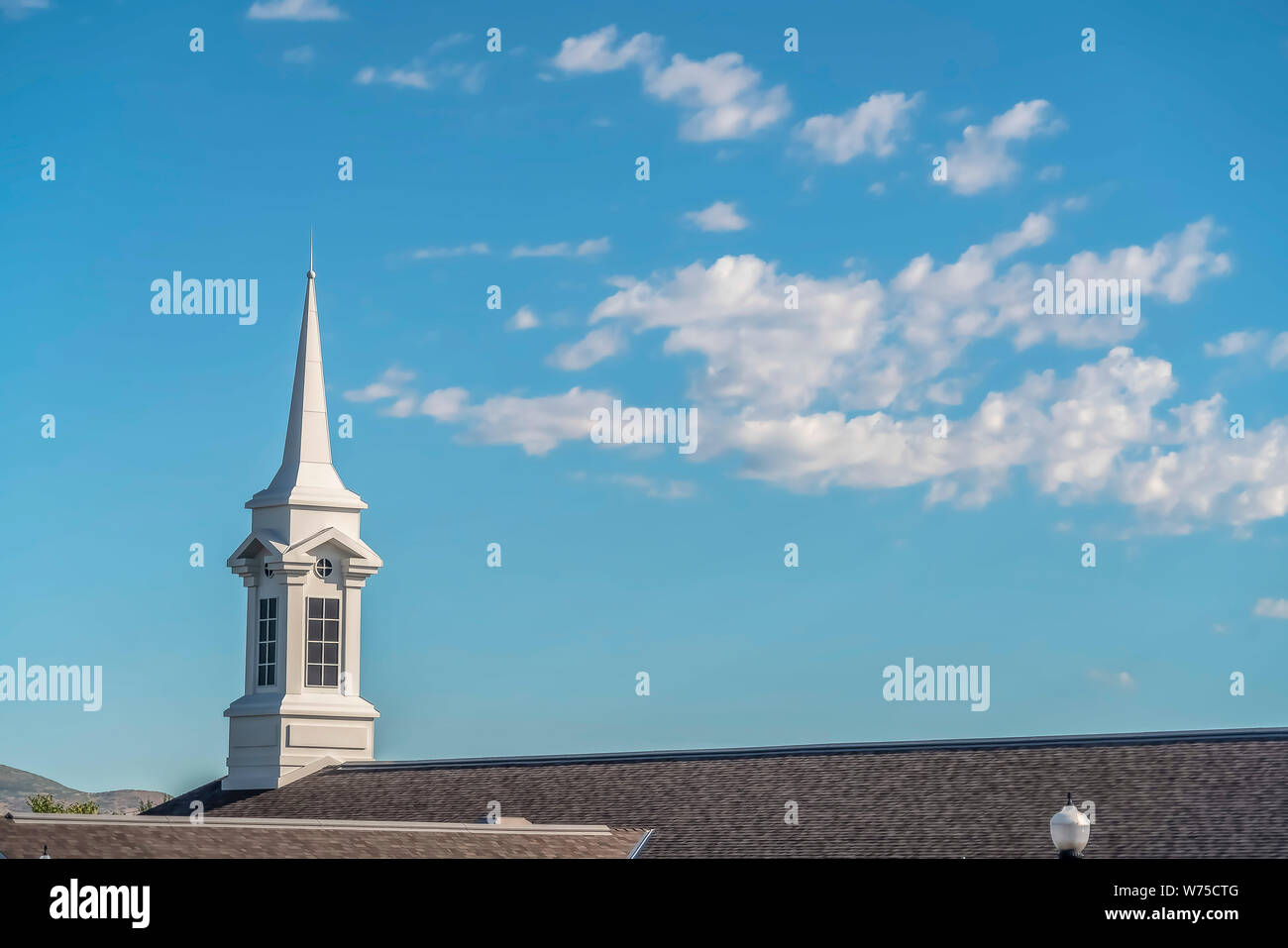 White steeple and dark roof of a church with blue sky and clouds ...