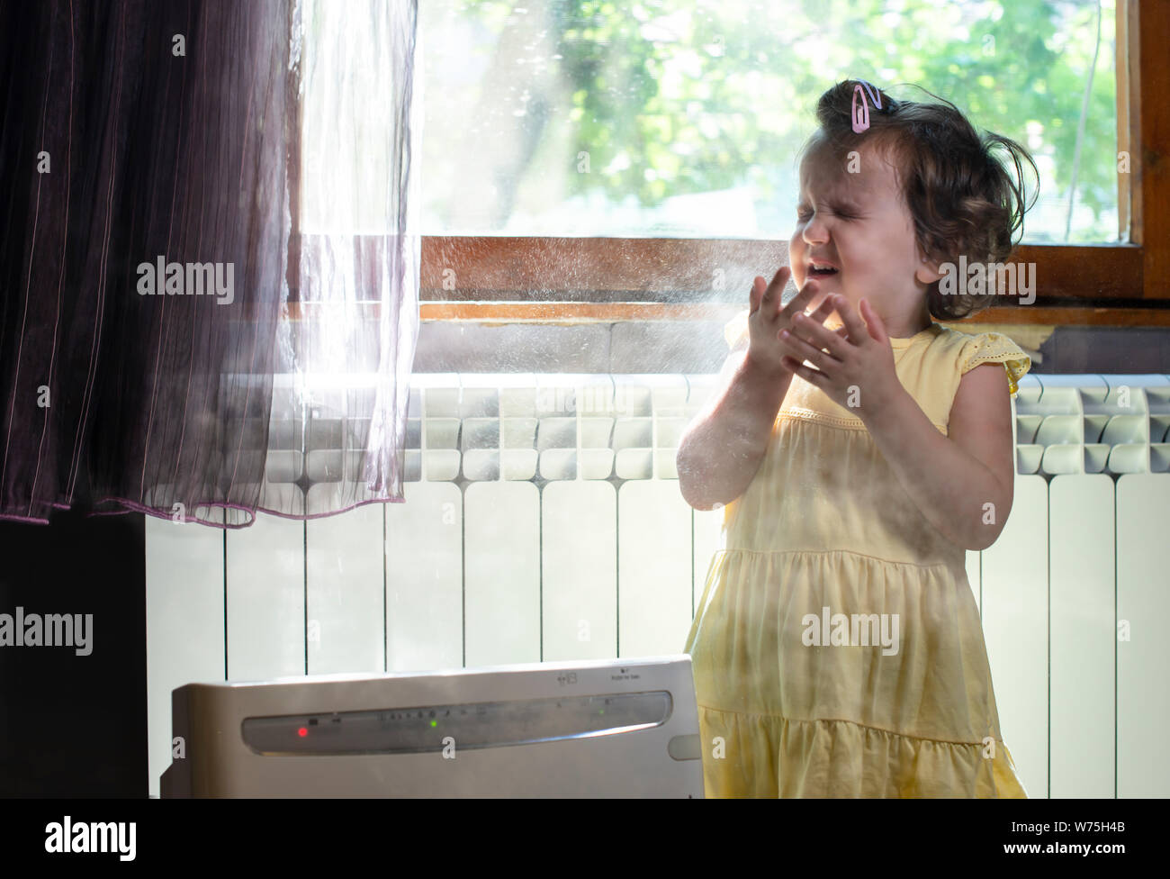 Little girl in a dusty room. Air purifier and coughing kid. Dust in the air. Allergy concept. Stock Photo