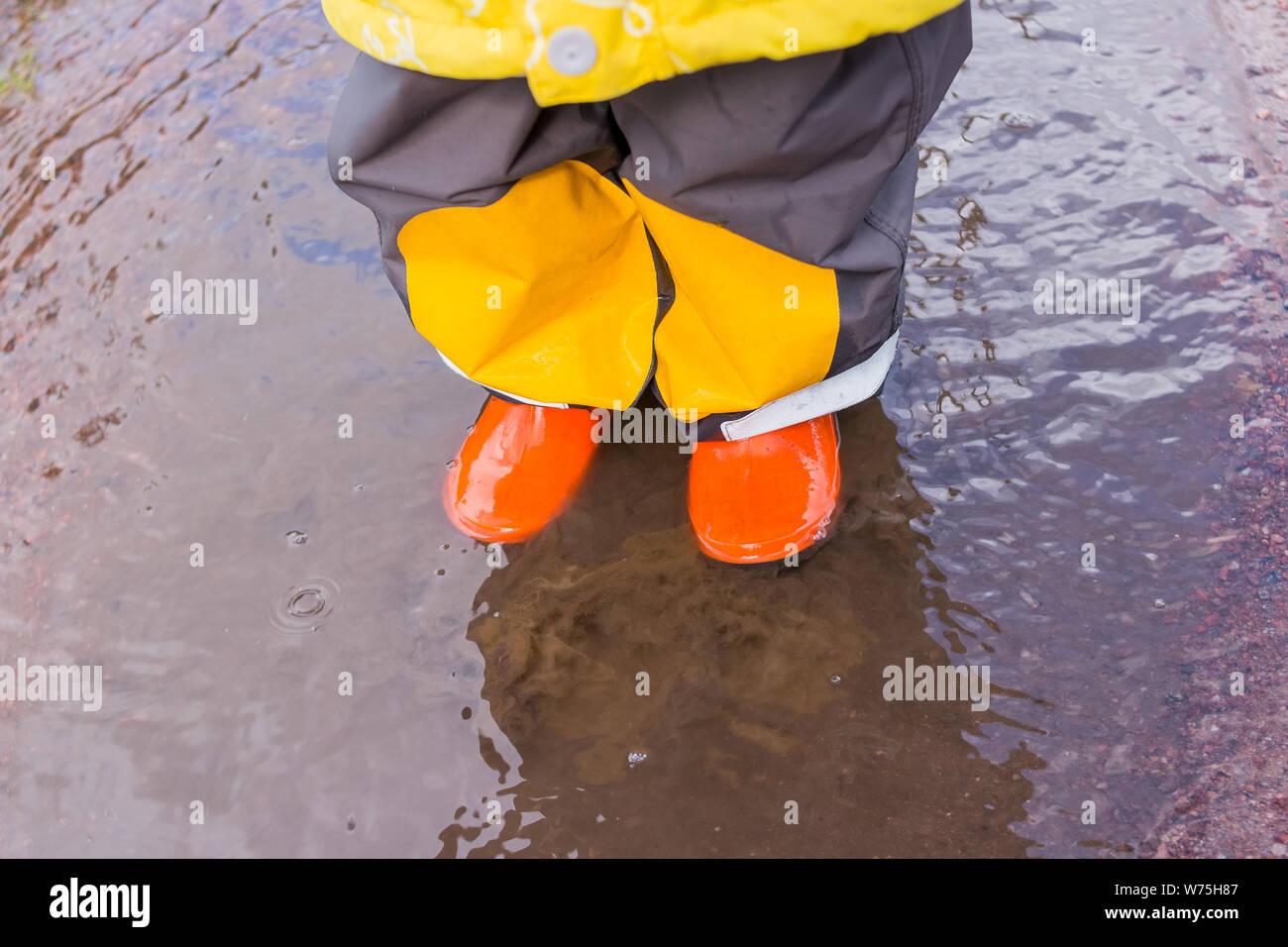 legs of child in orange rubber boots jumping in the autumn puddles
