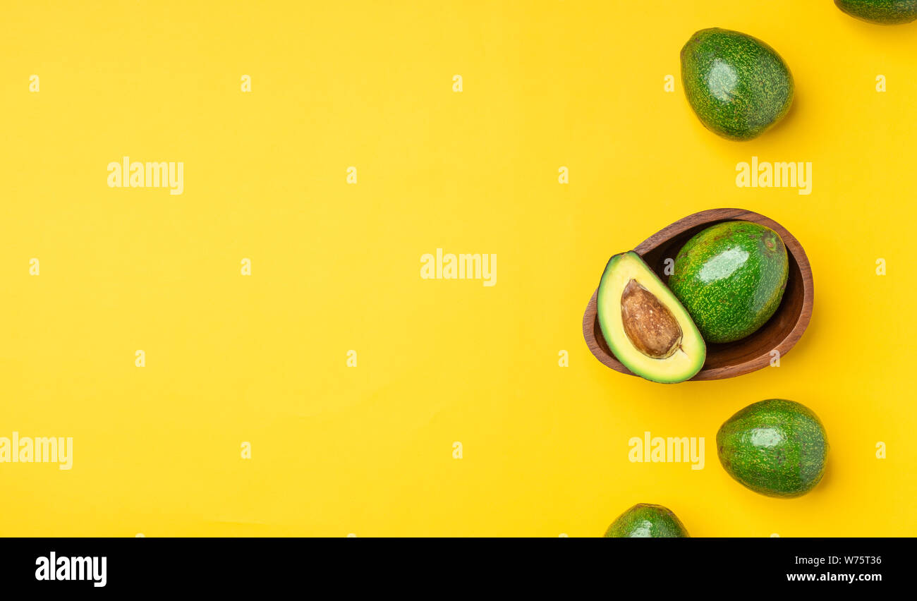 organic avocados half cut with seed and whole fruit in wood bowl on yellow table background.Healthy super foods for diet.Fresh vegetable from farm.ket Stock Photo