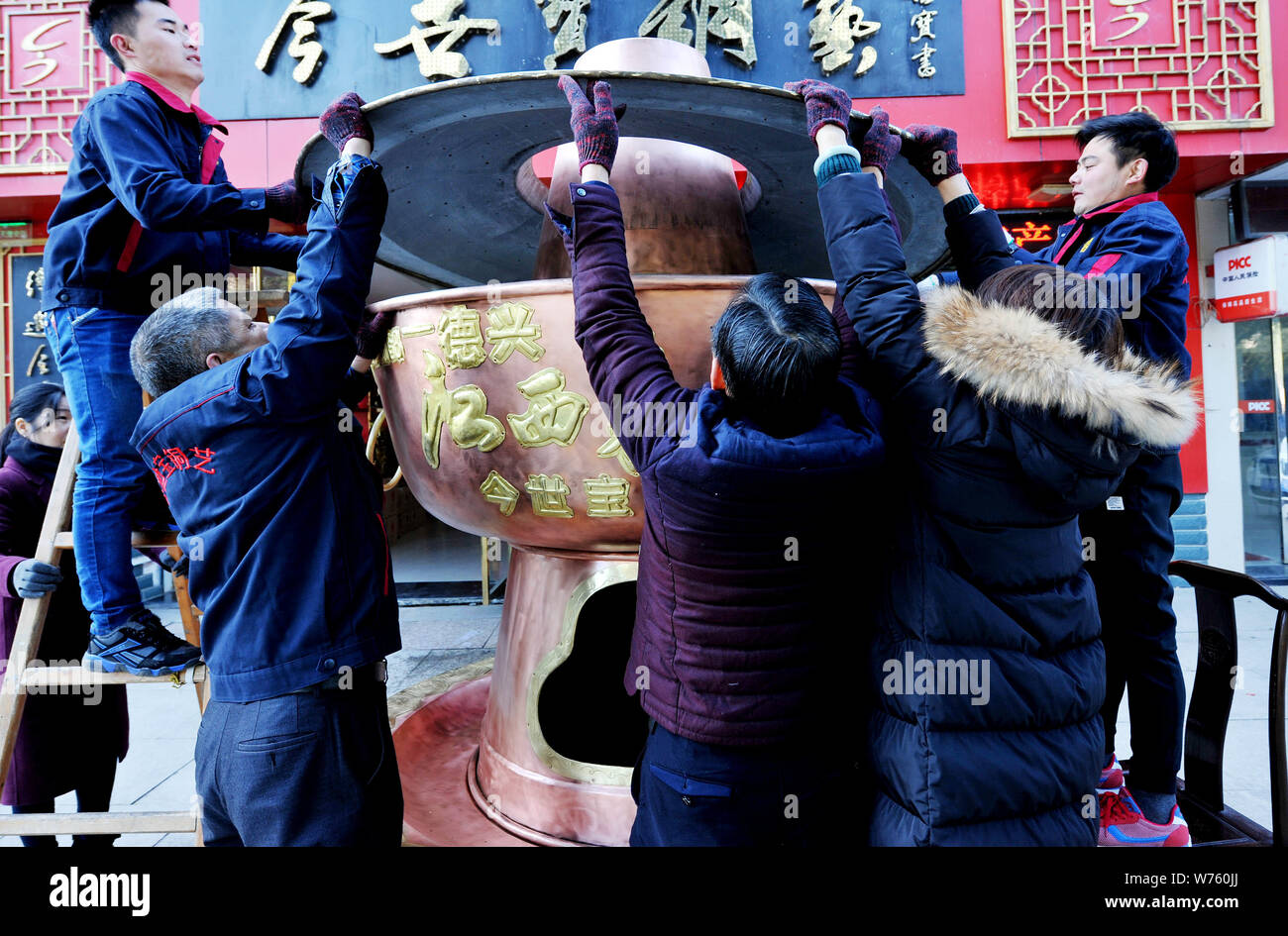 Chinese employees move a huge hotpot weighing over 400 kilograms with a height of 3 meters made of red copper to the front of a store in Dexing city, Stock Photo