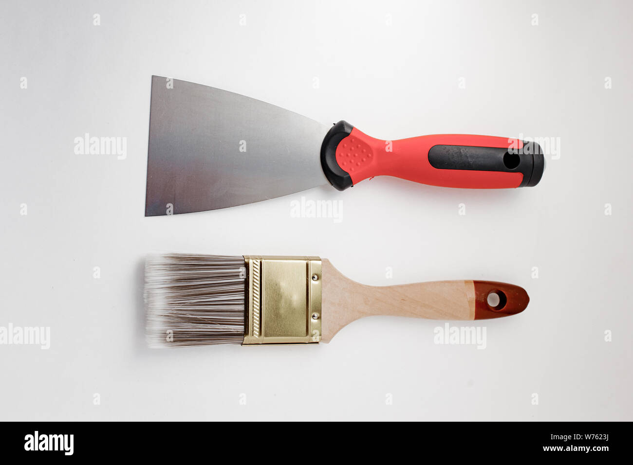 Metal spatula, trowel with plastic handle and paint brush on white background. Brush and spatula - paint tools on white background top view. Stock Photo