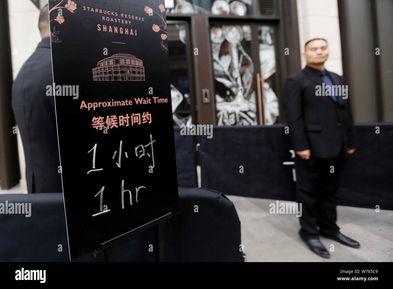 A security guard stands next to a signboard showing approximate waiting time outside the world's largest Starbucks Reserve Roastery in Shanghai, China Stock Photo
