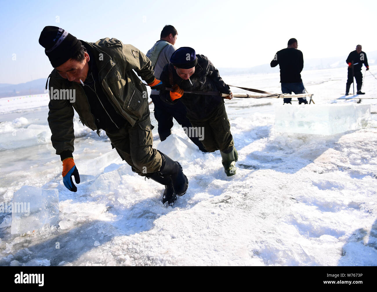 Chinese workers drag an ice block as others chisel it on the frozen ...