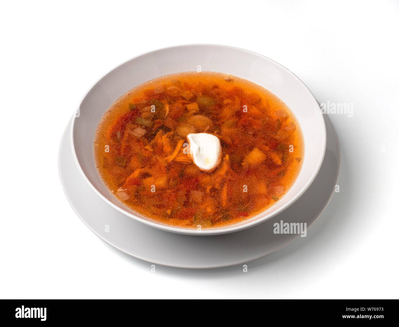Soup with chicken meat, potatoes, carrot, tomatoes in bowl. Plate of orange red russian-style soup isolated on white. Isolated on white with clipping path. Stock Photo