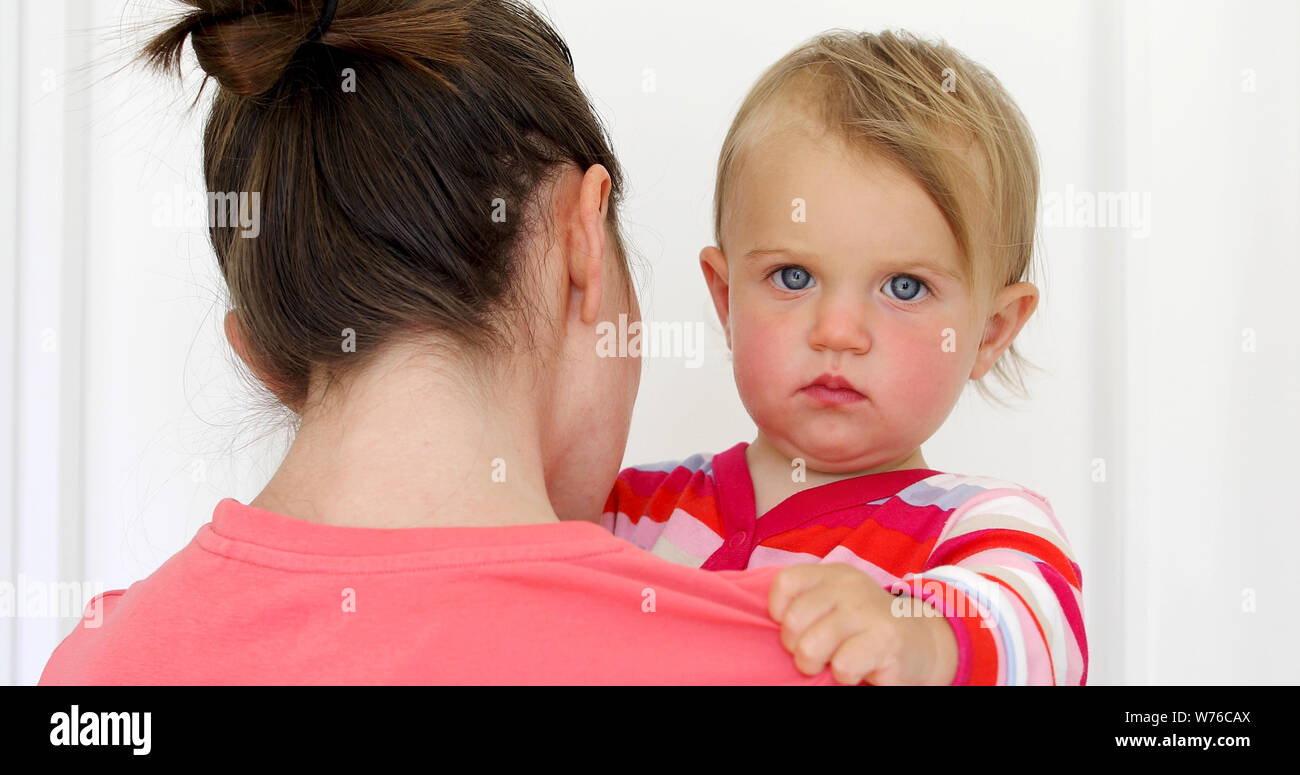 Serious child with red cheeky in hands of mother Stock Photo