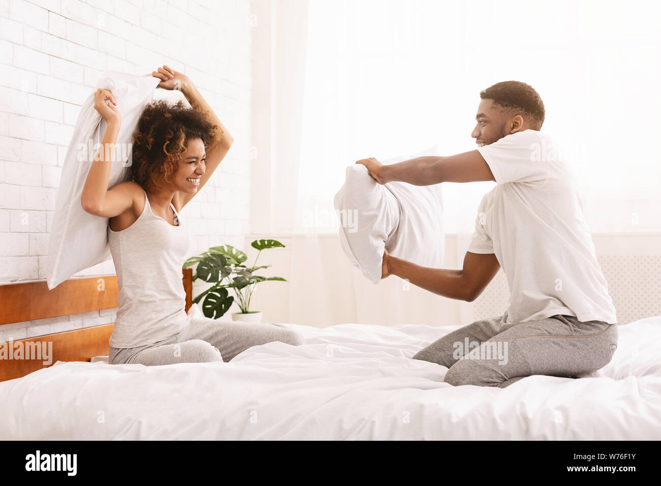 Cheerful loving couple is fighting by pillows in bed. Stock Photo