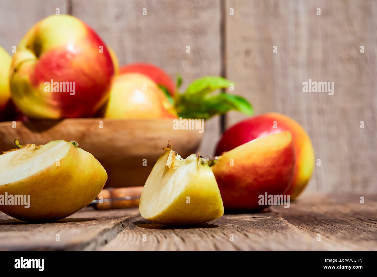 Fresh red apples with green leaves on a wooden old table. On a wooden background with sliced apple. Free space for text. soft focus Stock Photo