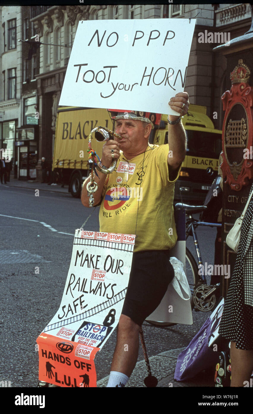 A one man protest band seated on a busy street corner protesting railtrack holding a sign reading No PPP Toot you Horn Stock Photo