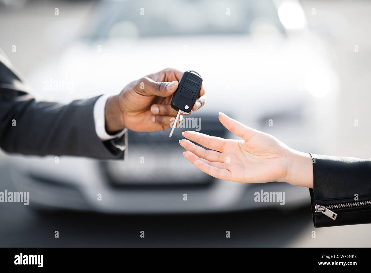 Car salesman handing over keys for new car to young woman Stock Photo