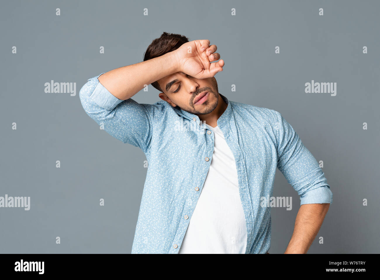 Exhausted hispanic man wiping sweat off forehead on gray background Stock Photo