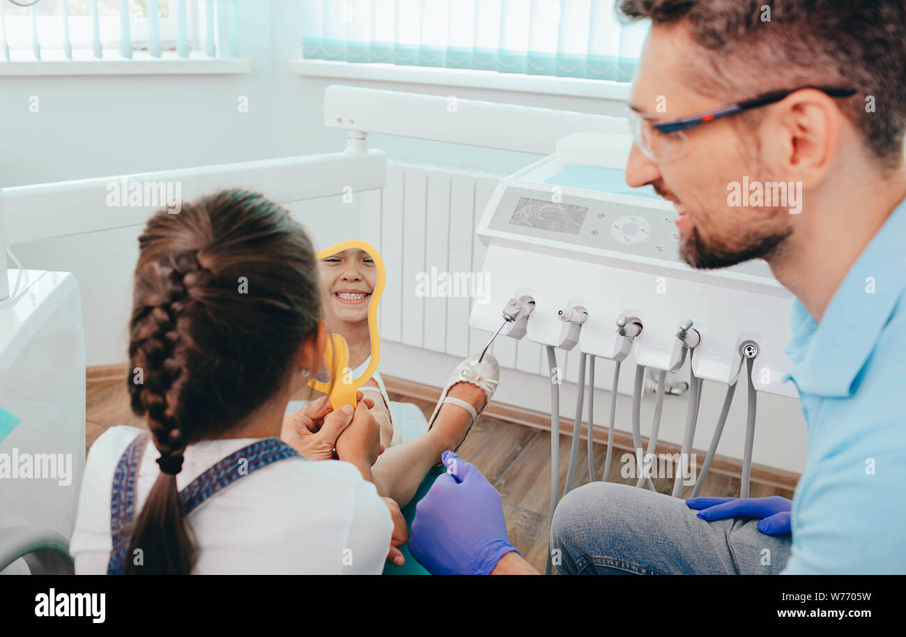 Little girl holding mirror and looking on her perfect healthy teeth