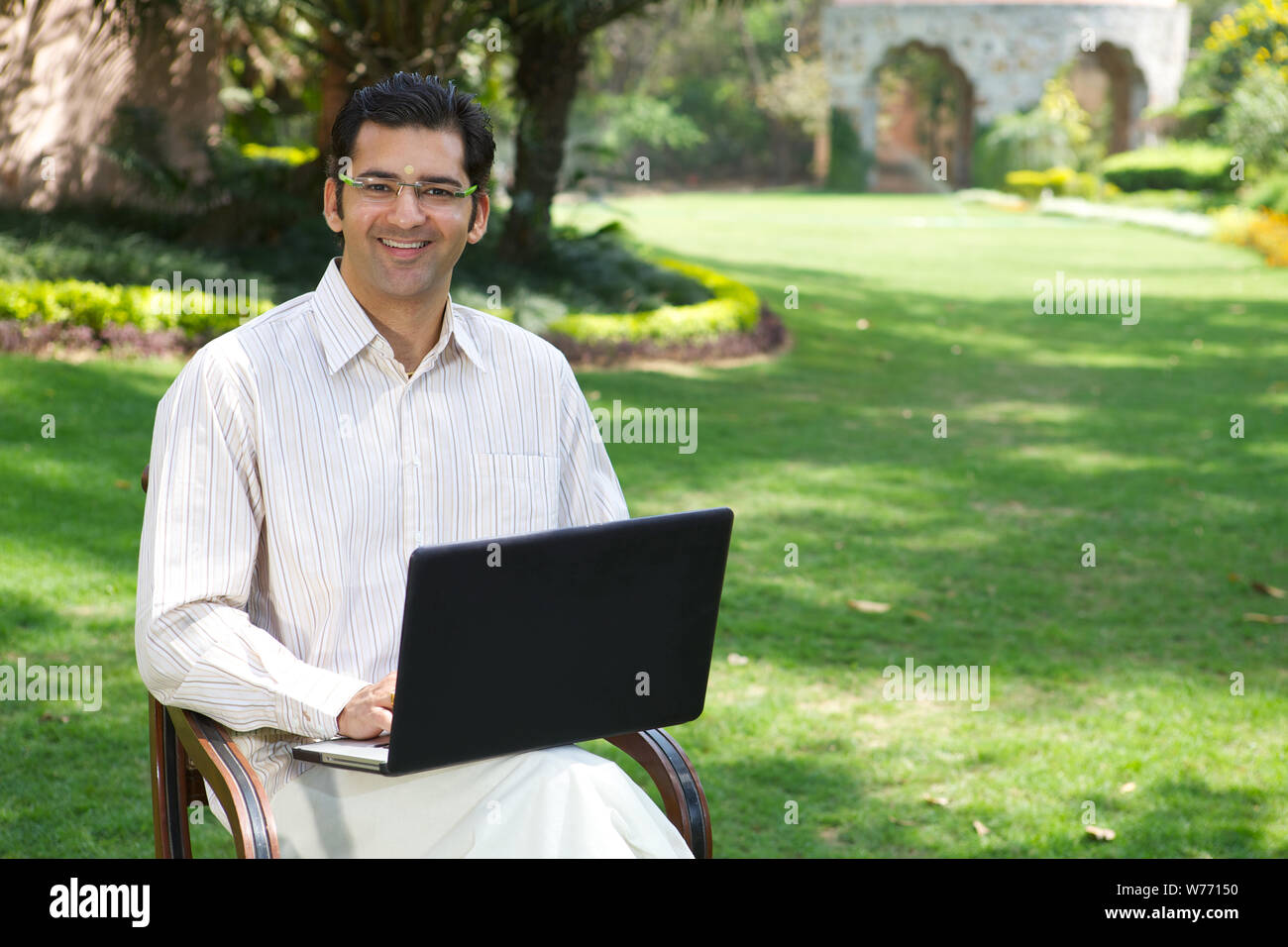 South Indian man working on a laptop in a lawn Stock Photo