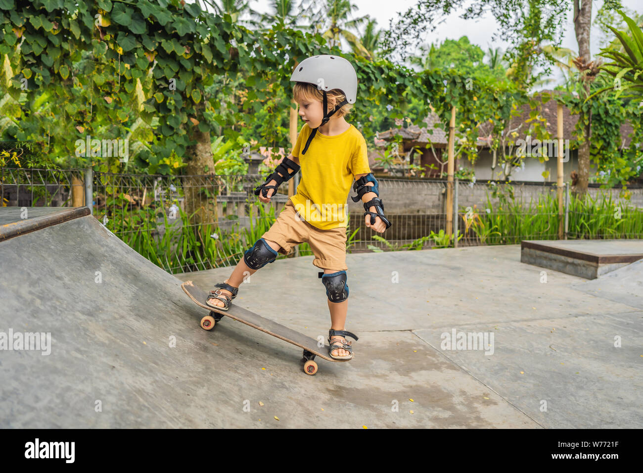 Athletic boy in helmet and knee pads learns to skateboard with in a