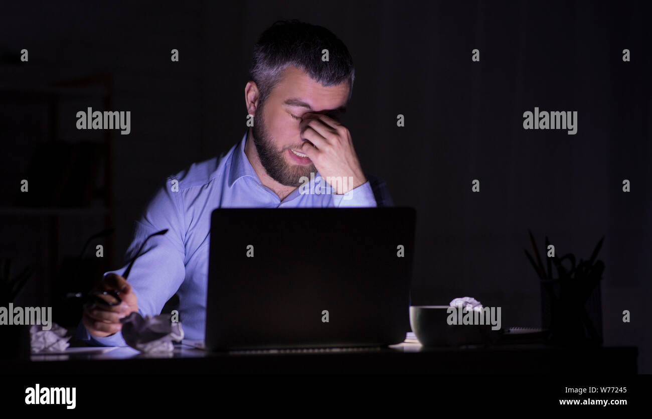Tired man is working on laptop in darkness Stock Photo