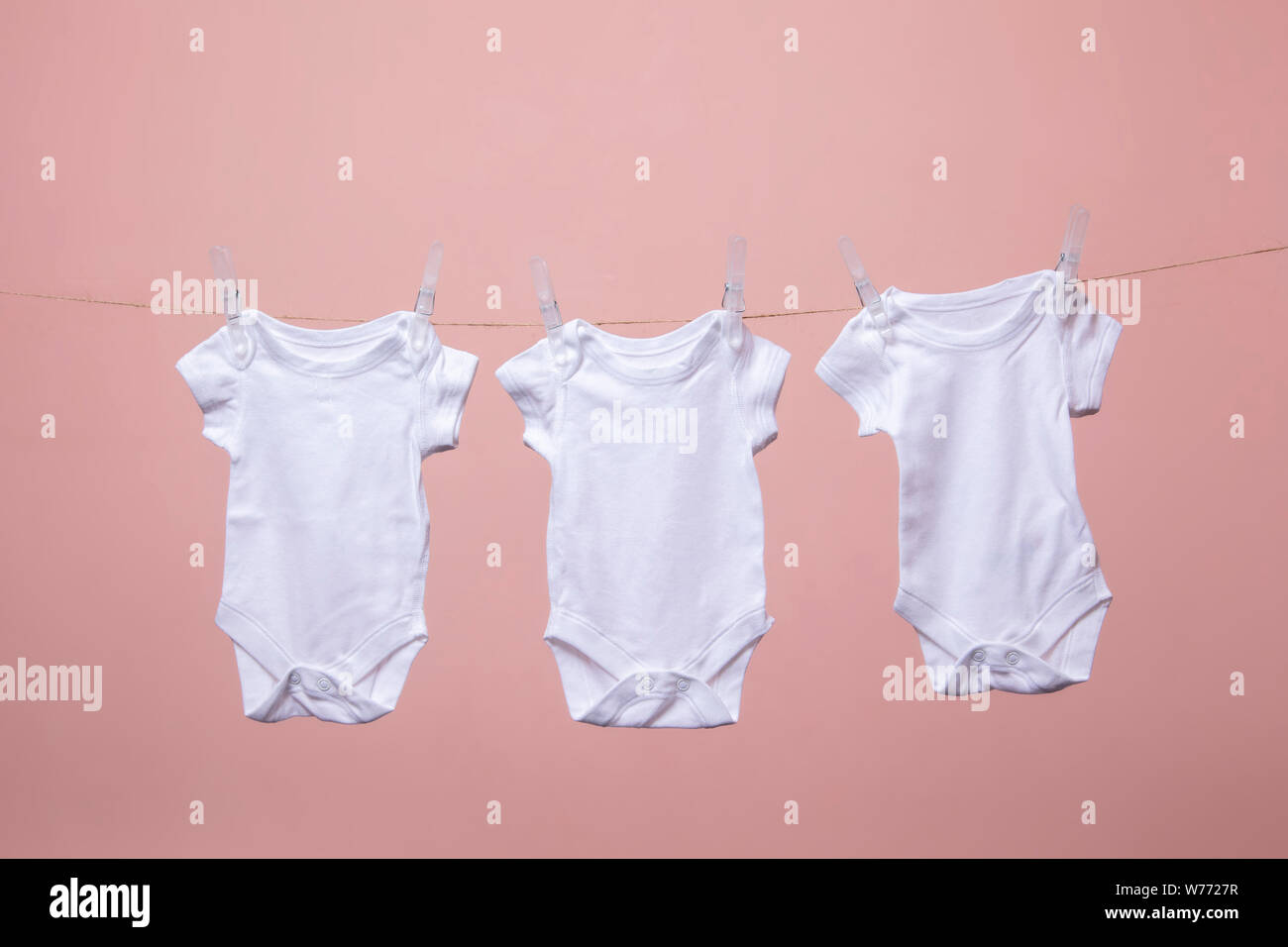 White baby body suit hanging from a line against a pink background Stock Photo