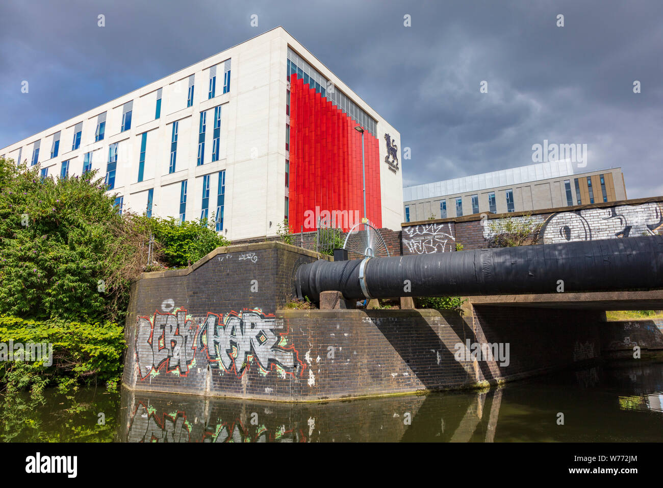 Birmingham City University red and white building on Curzon street hit by the summer light against dark clouds makes dramatic views on the Digbeth Branch Canal, Stock Photo