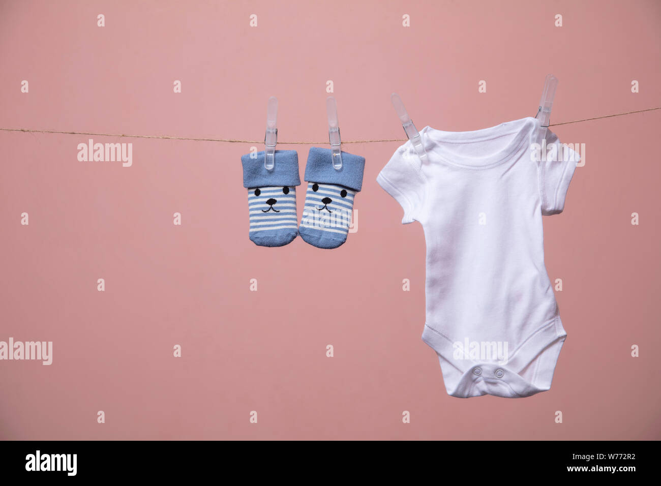 White baby body suit hanging from a line against a pink background Stock Photo