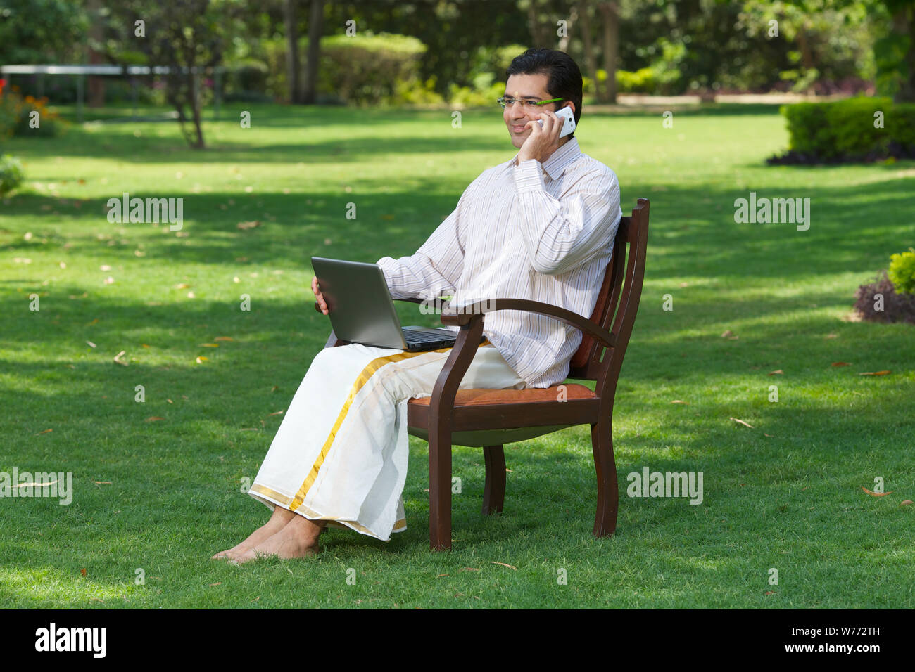 South Indian man talking on mobile phone and using laptop Stock Photo