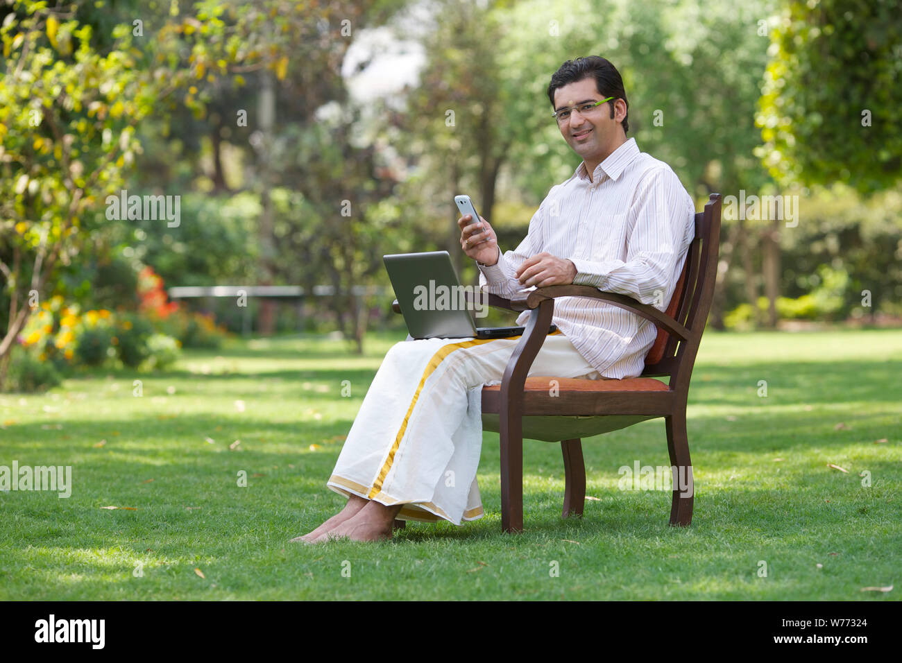 South Indian man text messaging on mobile phone and using laptop Stock Photo