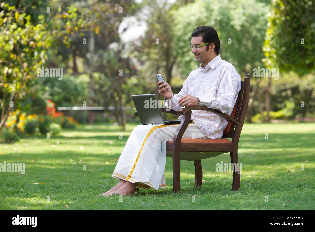 South Indian man text messaging on mobile phone and using laptop Stock Photo