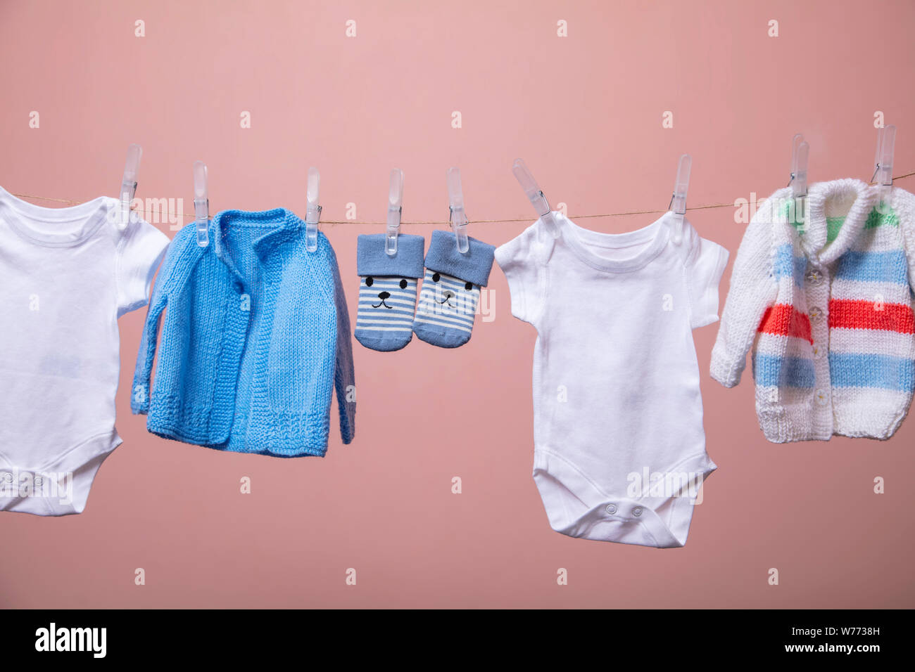 New born baby grows, jumpers, socks hanging on a clothes line against pink Stock Photo