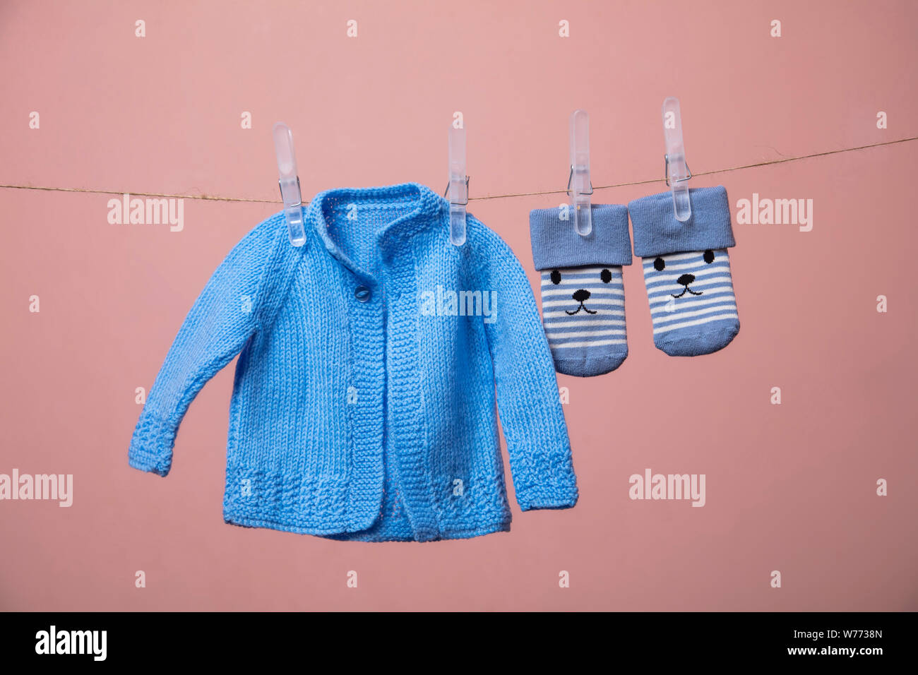 knitted new born baby jumper and socks hanging on a clothes line against pink Stock Photo