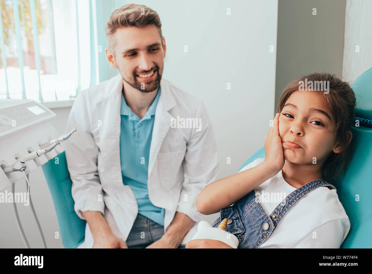 mixed race little girl showing toothache at camera. Sadness child in dental chair Stock Photo