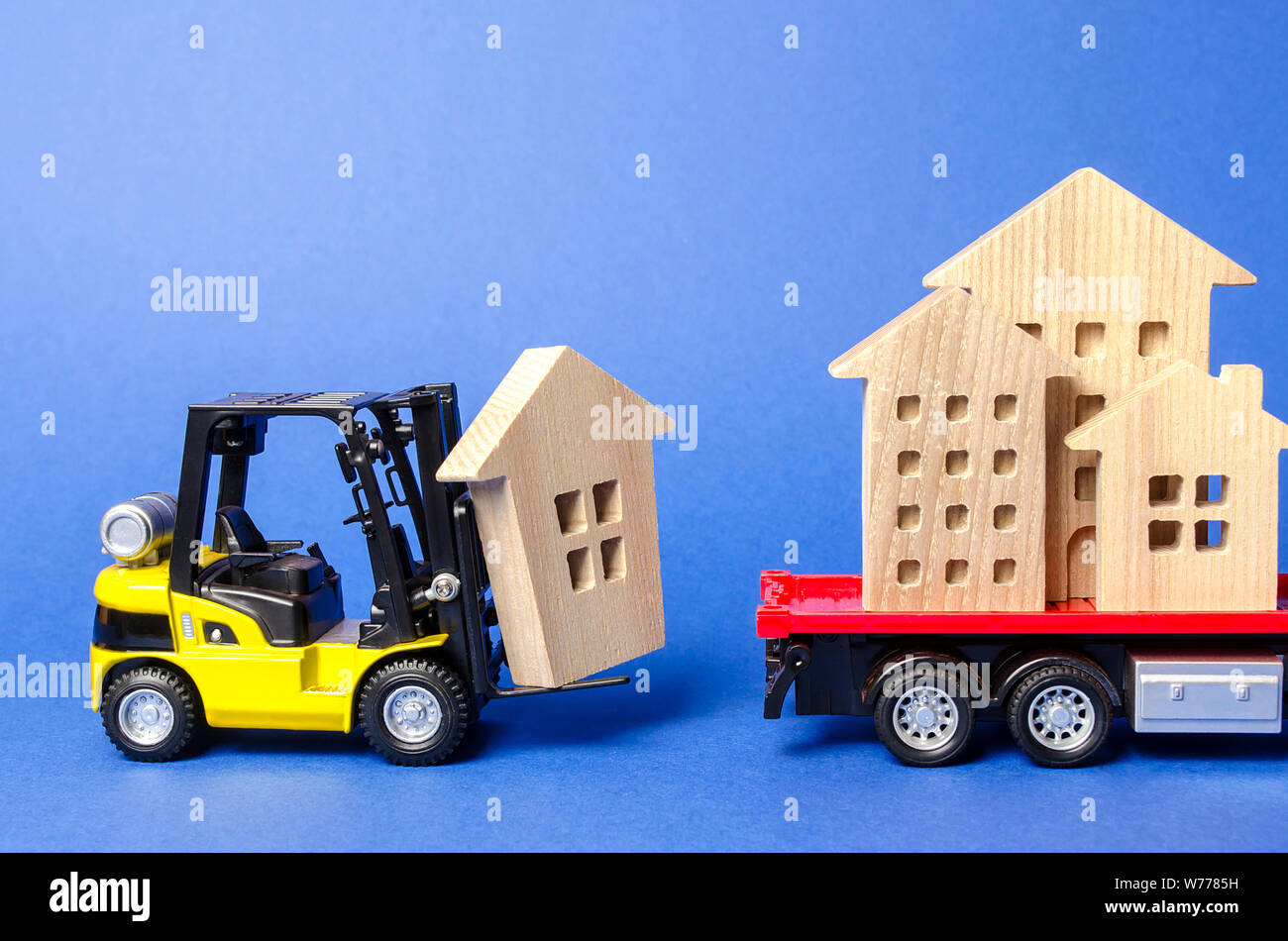 A yellow forklift loads a wooden figure of a house into a truck. Concept of transportation and cargo shipping, moving company. Construction of new hou Stock Photo