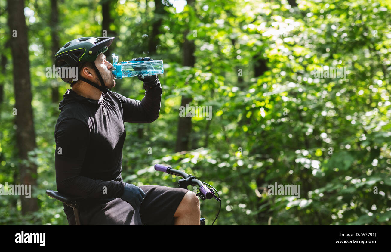 Male cyclist sitting on bike and drinking water in forest Stock Photo