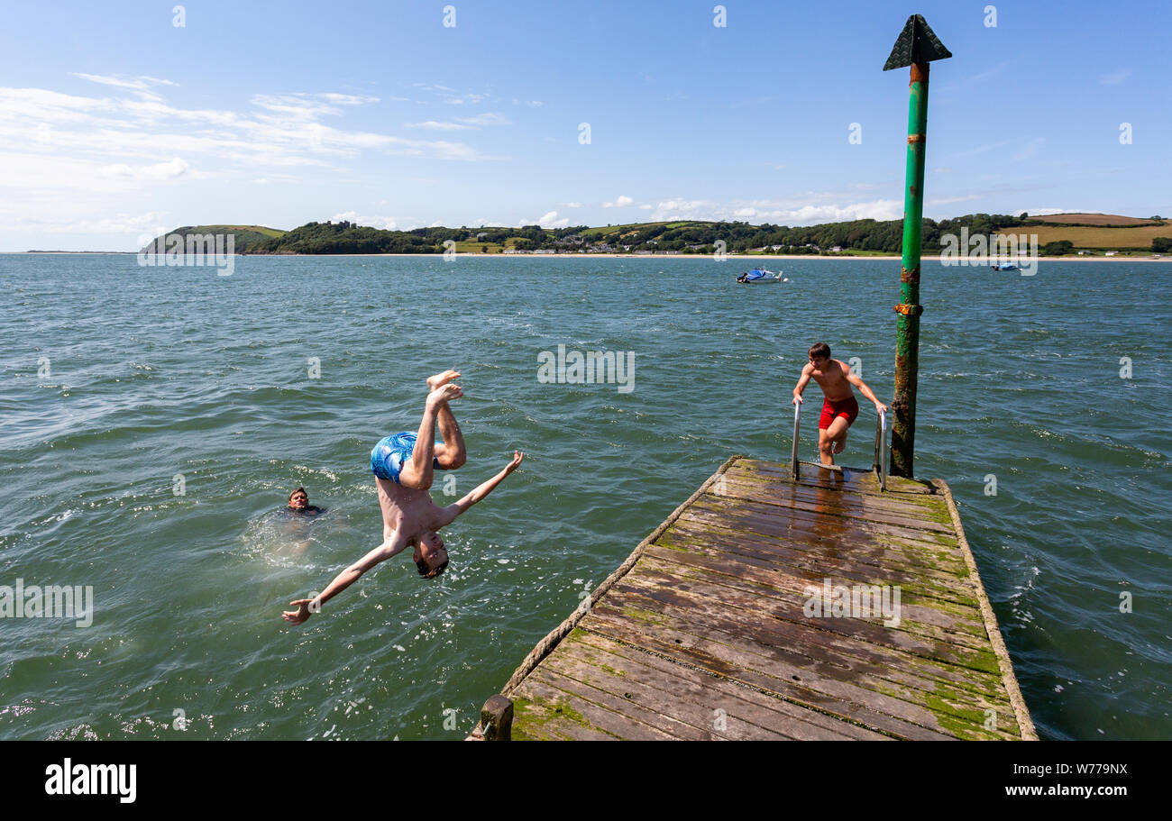 Three boys jumping and diving into the sea at Ferryside, Carmarthenshire on hot, sunny summer day with view across to Llansteffan Stock Photo