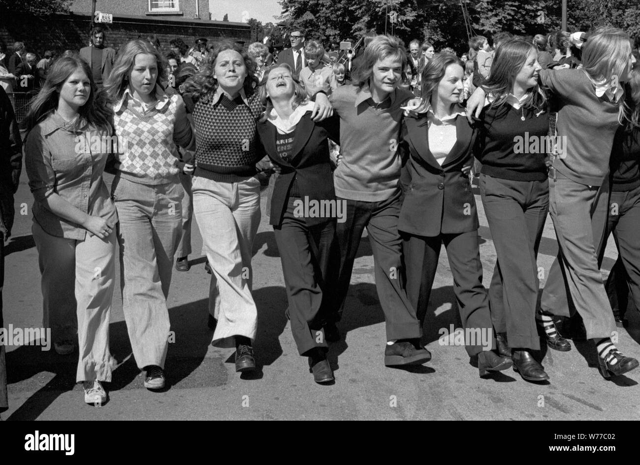 Teenage girls arms linked together having fun, looking stylish 1970s at the Durham Coal Miners annual gala  County Durham UK 70s.  One boy in the middle. All the girls are wearing trousers.1974 England HOMER SYKES Stock Photo