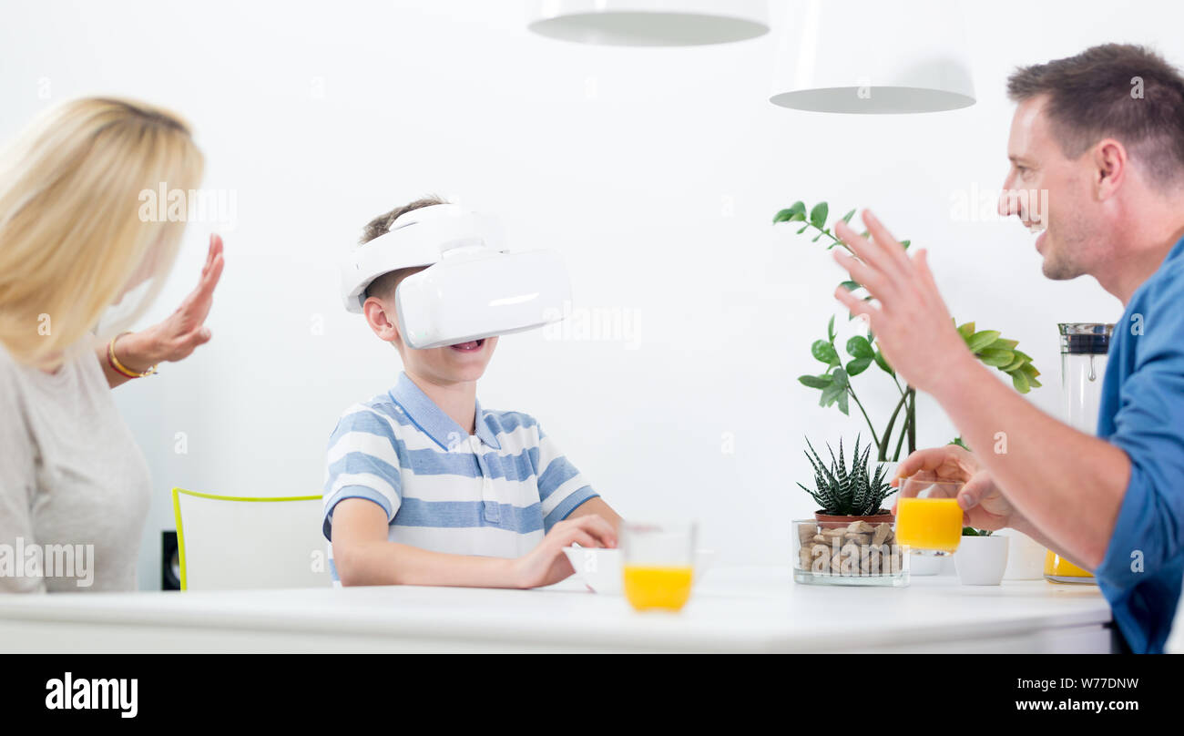 Happy caucasian family at home at dinning table, having fun playing games using virtual reality headset Stock Photo