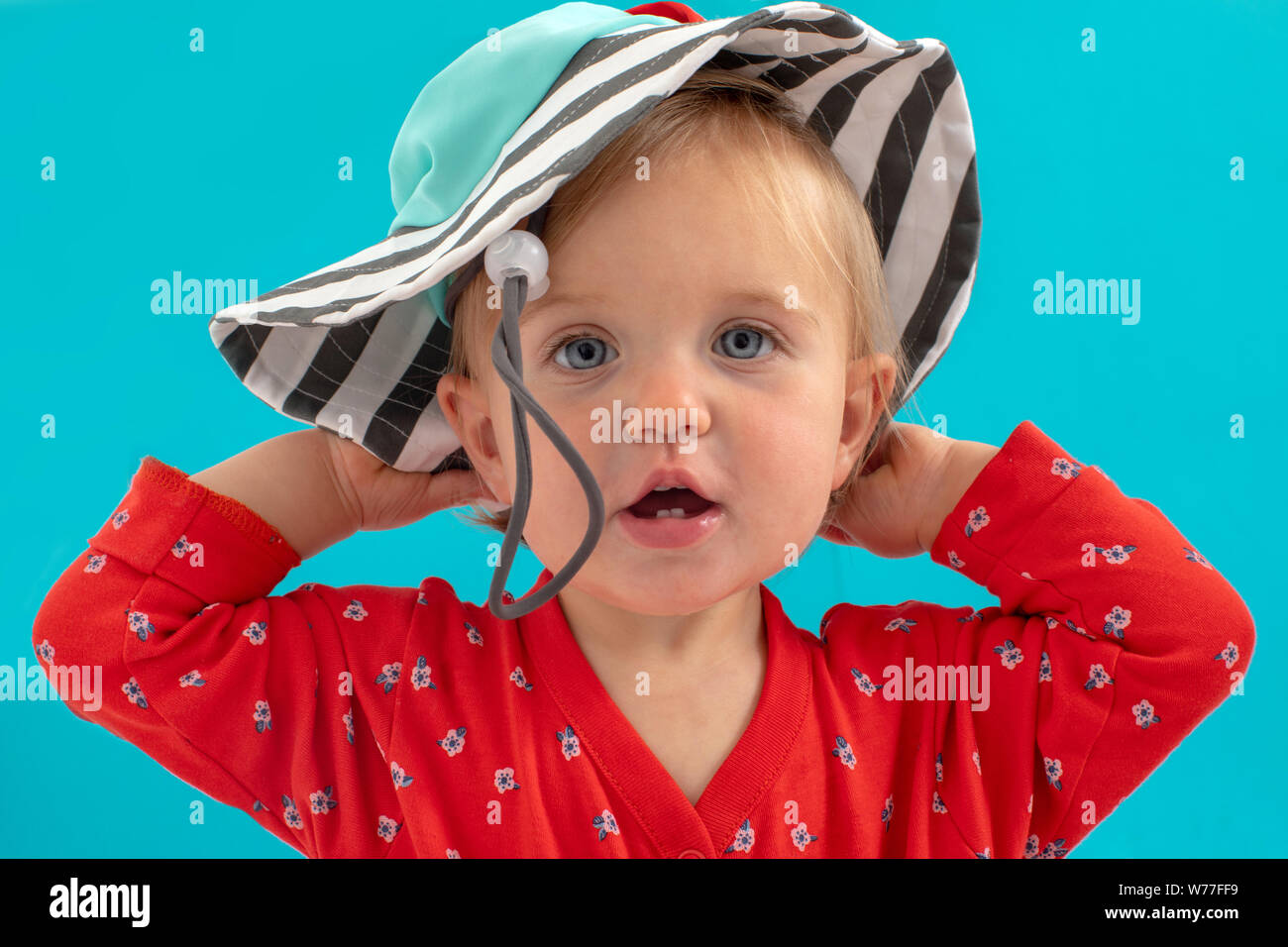 Little girl putting on hat over blue Stock Photo