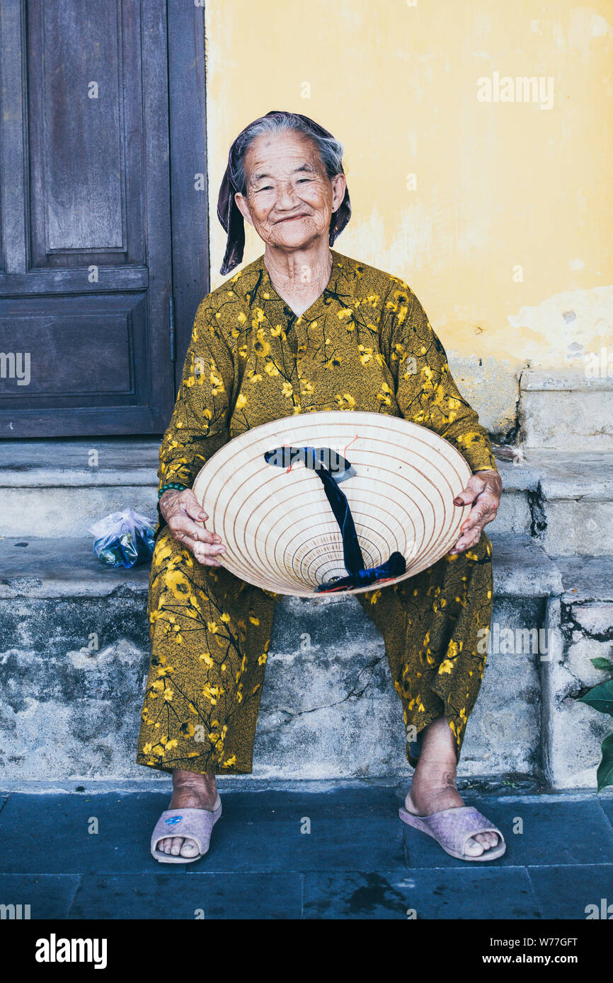 Hoi An, Vietnam - June 2019: portrait of old Vietnamese woman holding traditional conical hat and smiling Stock Photo
