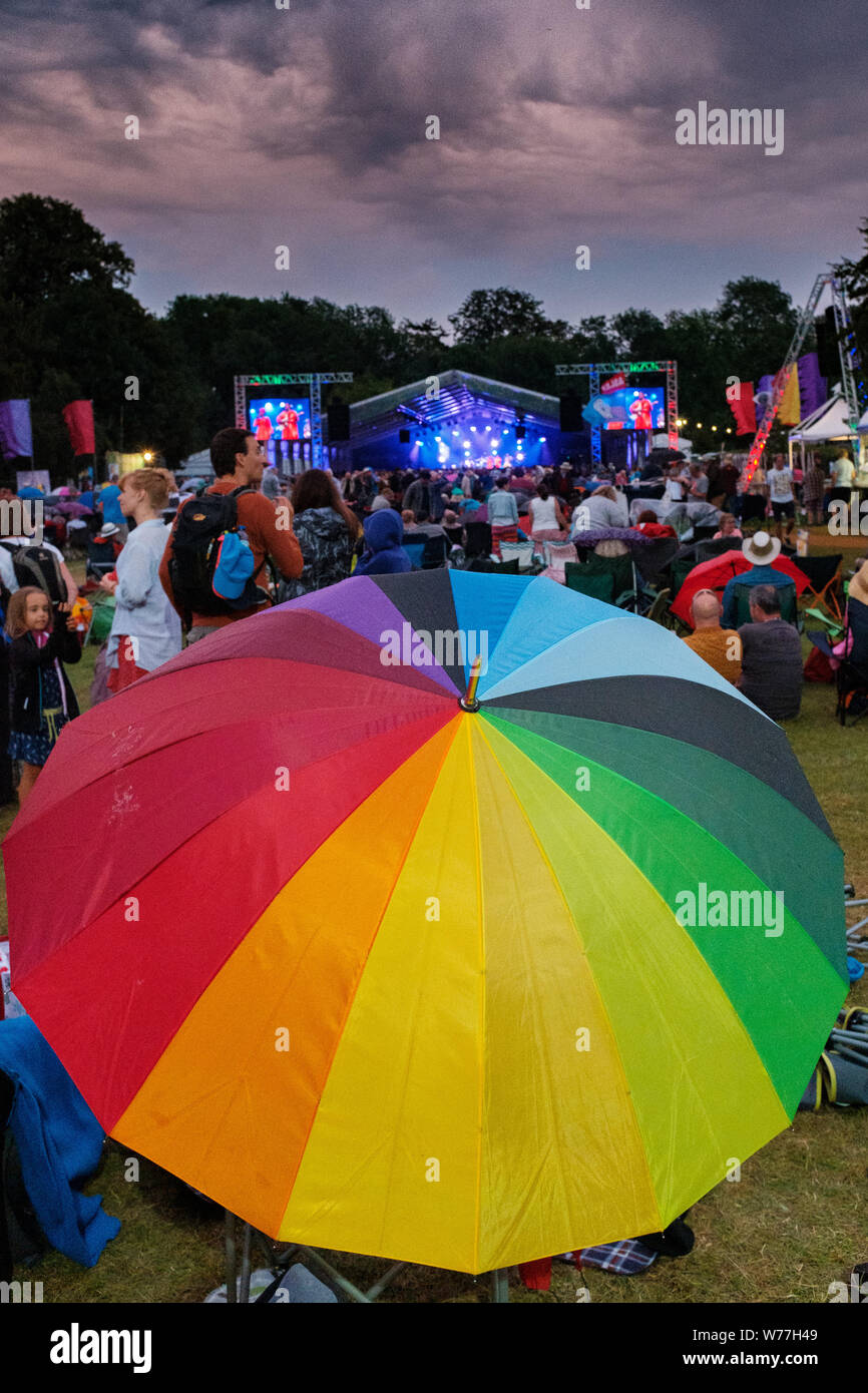 Cambridge, UK. 4th August 2019. A festival attendee opens a rainbow umbrella during slight rain showers at the Cambridge Folk Festival. Richard Etteridge / Alamy Live News Stock Photo