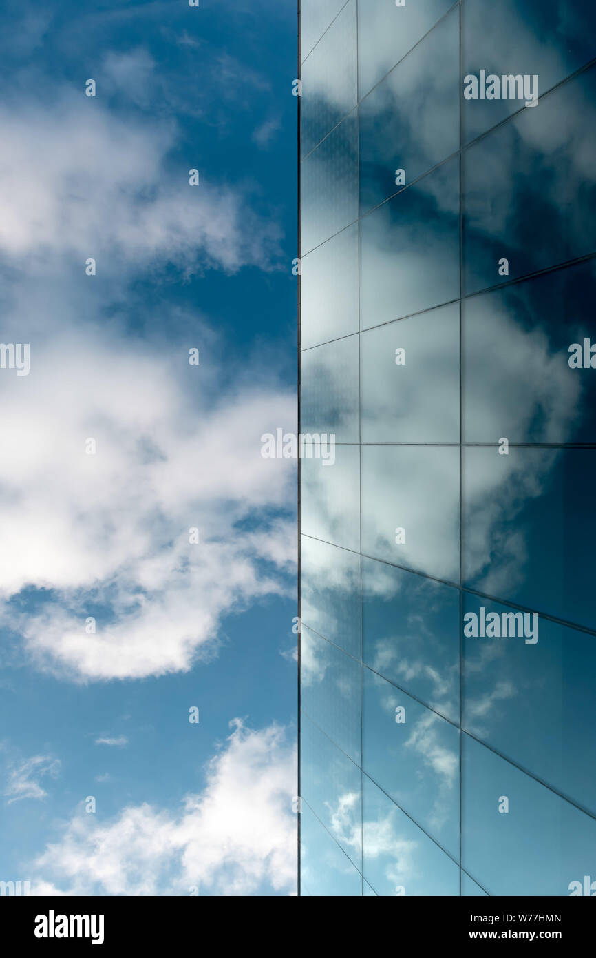 A blue sky and a modern blue glass facade in which clouds are reflected ...