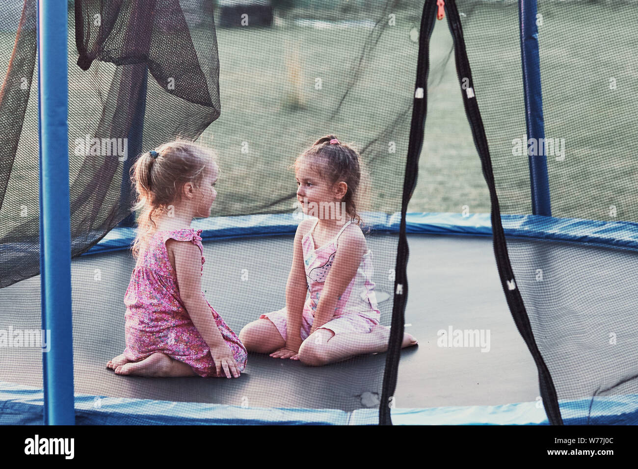 Two little cute girl talking, sitting and playing on trampoline in backyard on summer day Stock Photo