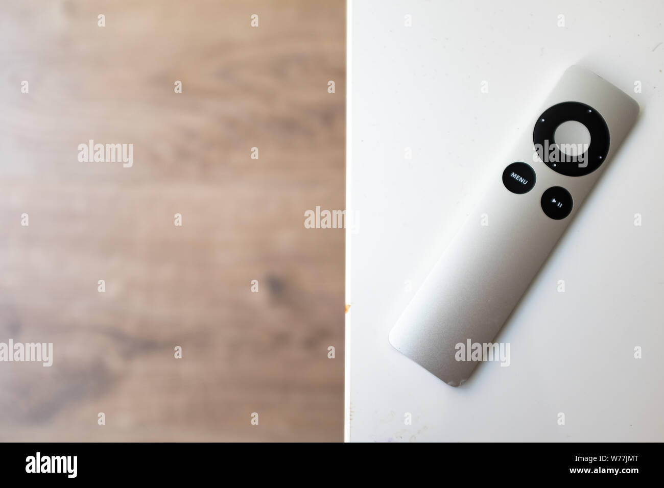 Grey remote control on a white table over a wooden blurry background Stock Photo