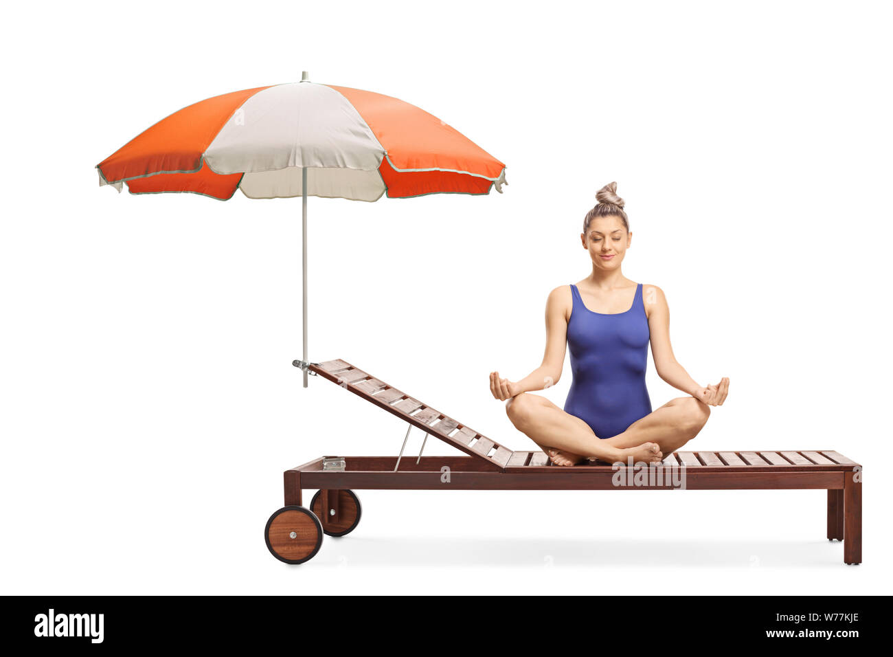 Young woman in a swimming suit meditating on a sunbed under umbrella isolated on white background Stock Photo