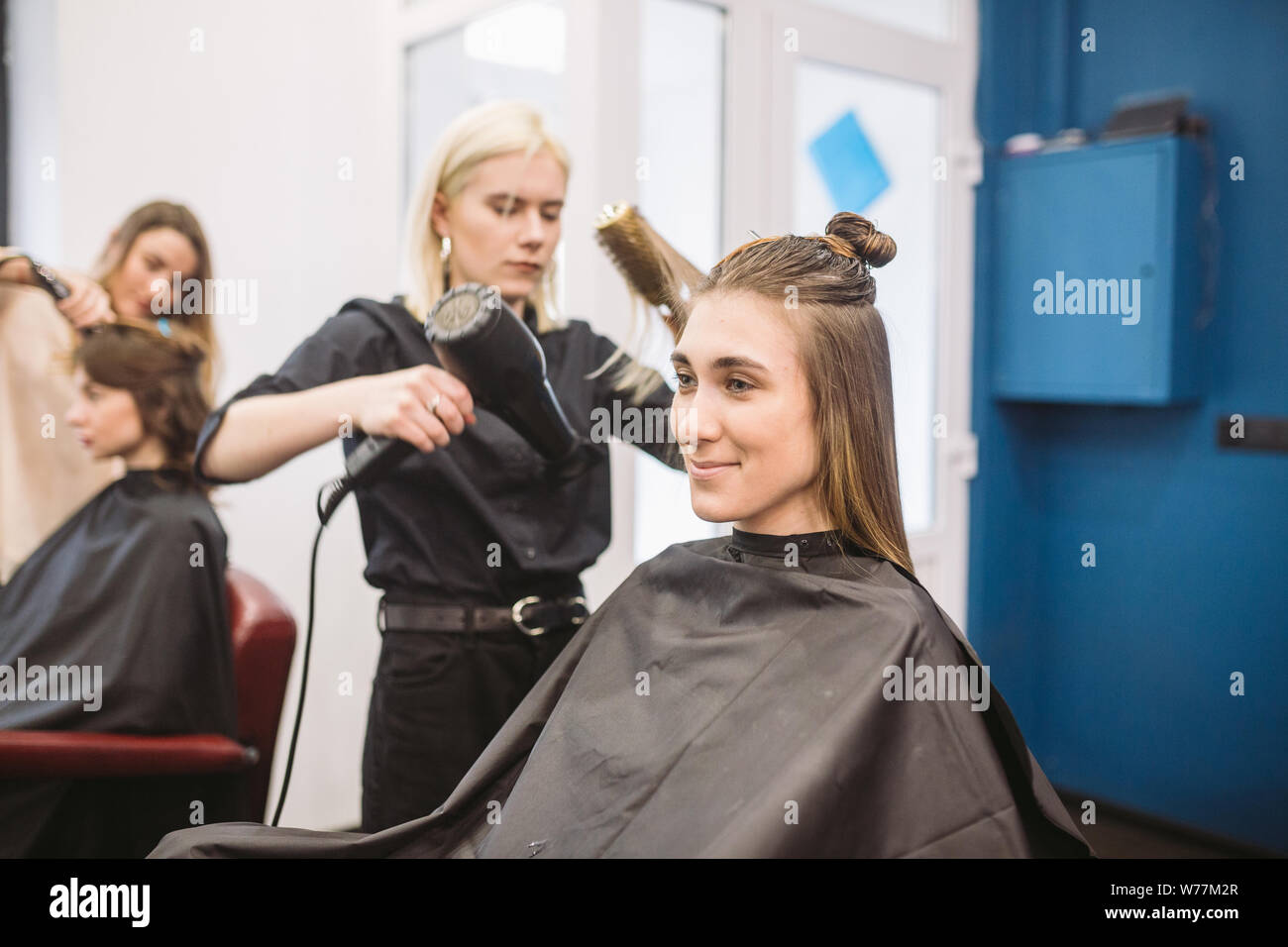 Portrait of happy woman at the hair salon. Professional hair styling concept. Hairdresser drying girl long hair using hairdryer and brush. Drying With Stock Photo